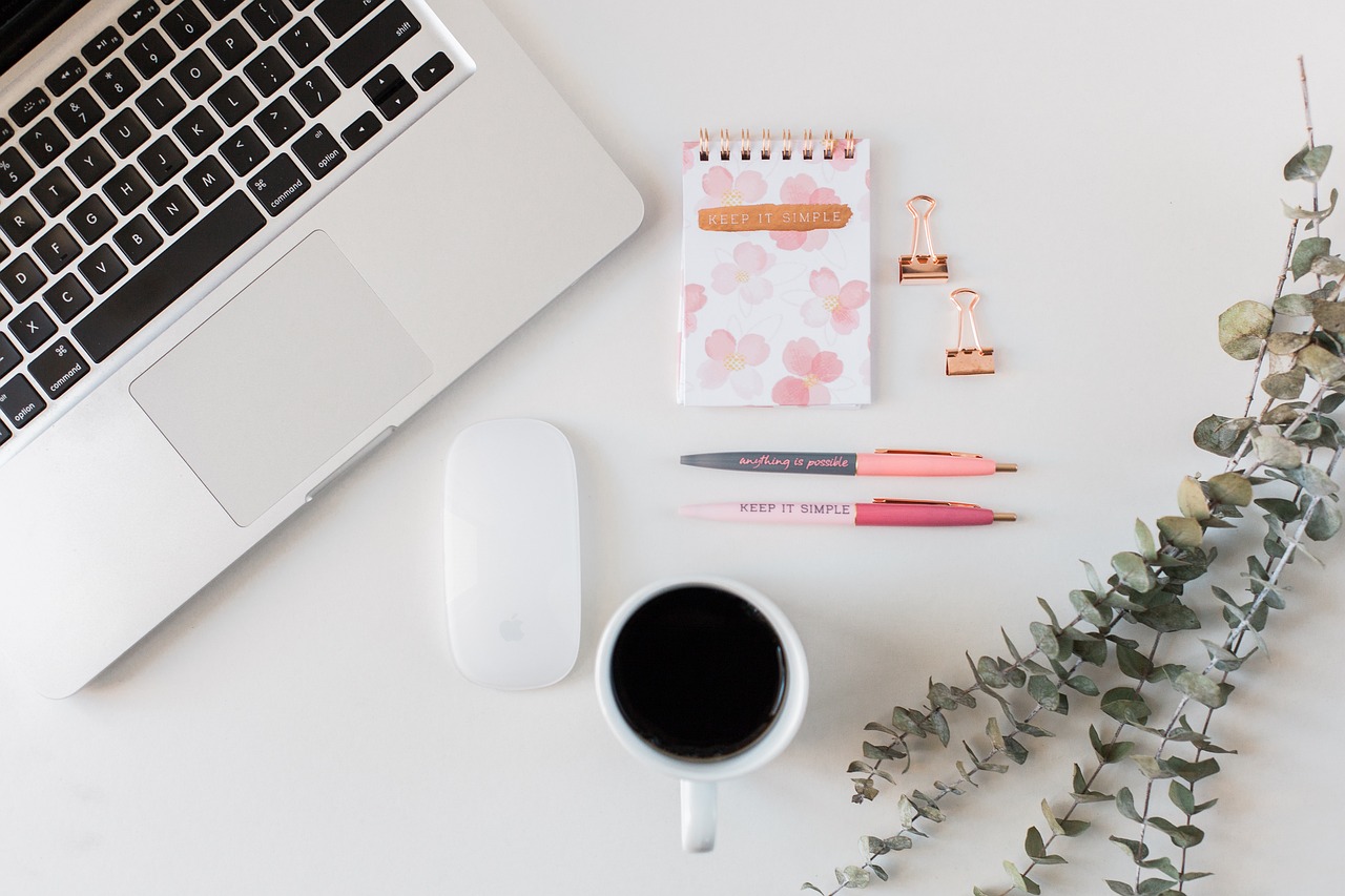 Das ist ein Foto von einem Laptop samt Laptopmaus, einer Tasse Kaffee und einem Notizbuch mit Stiften und Büroklammern. Das ist ein Foto von einem Laptop samt Laptopmaus, einer Tasse Kaffee und einem Notizbuch mit Stiften und Büroklammern.